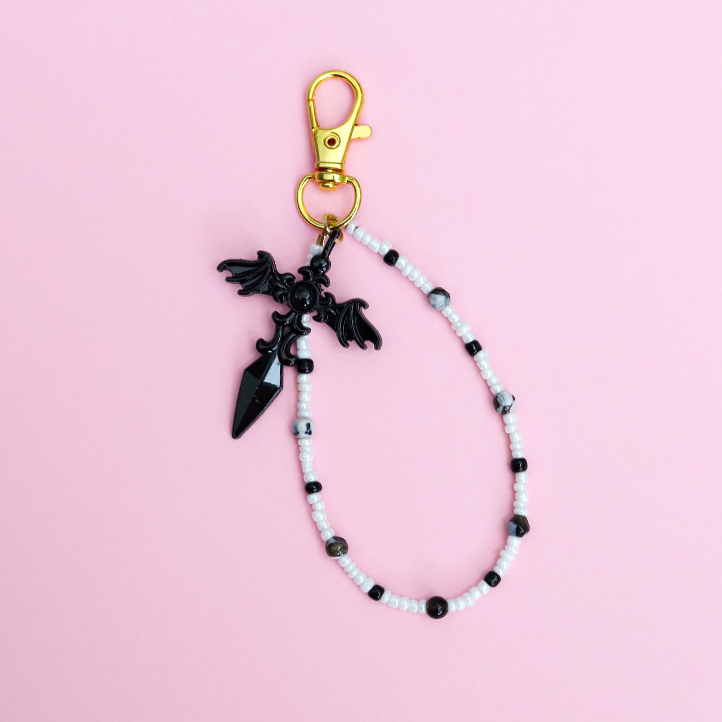 Keychain with black and white beads and black gothic cross pendant on a pink background