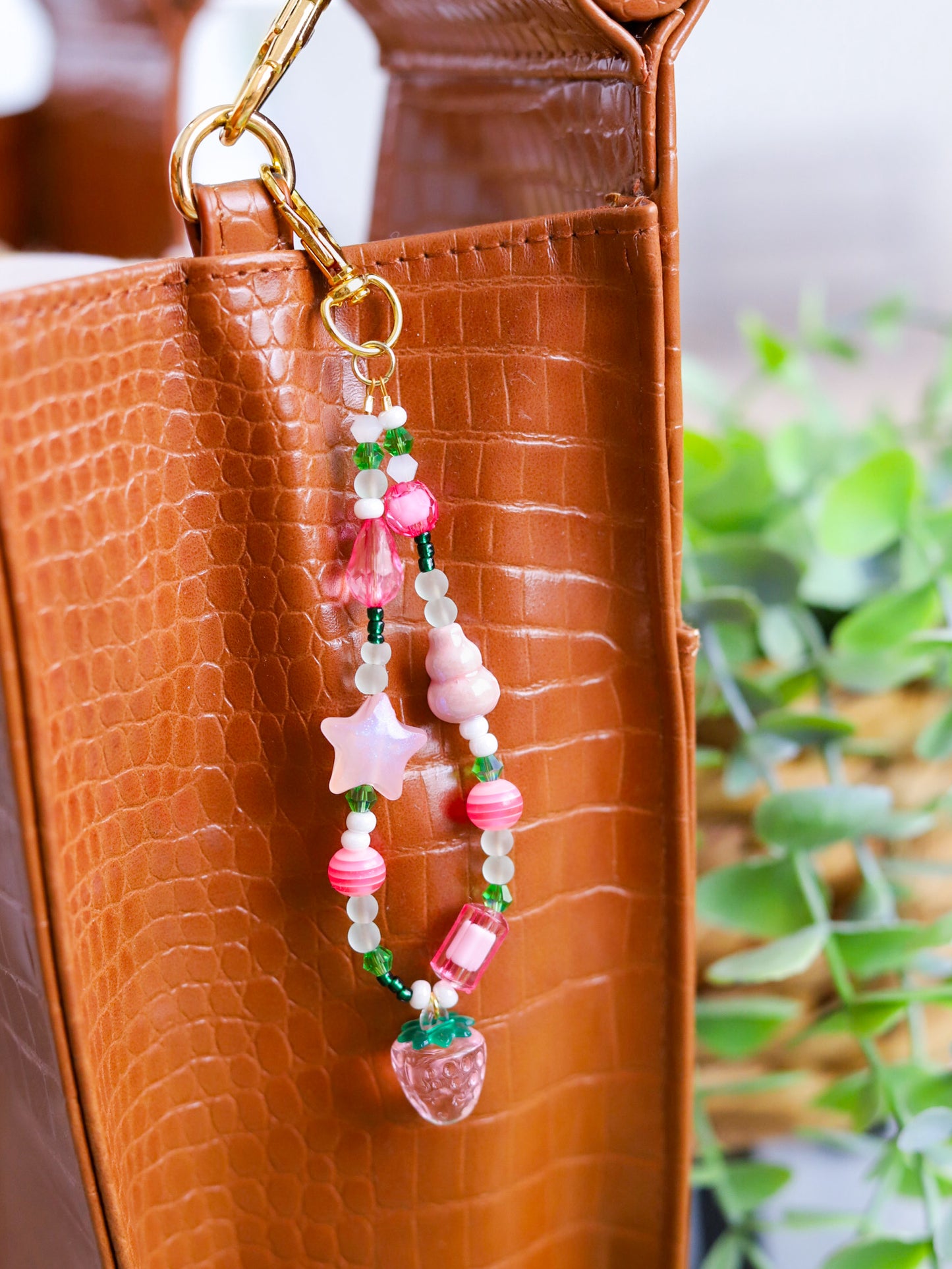 Beaded keychain with pink and green assorted beads and a light pink strawberry pendant hooked on a brown leather purse