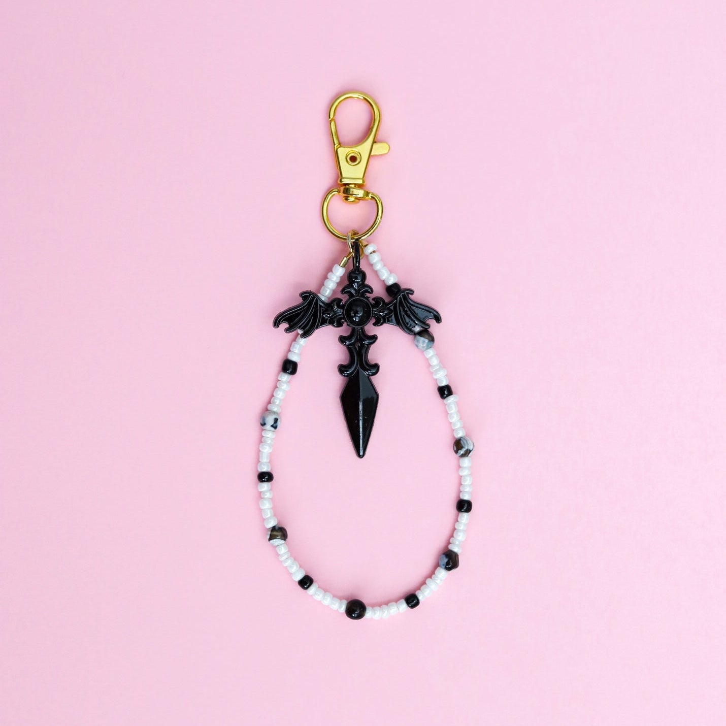 Keychain with black and white beads and black gothic cross pendant on a pink background