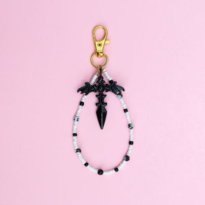 Keychain with black and white beads and black gothic cross pendant on a pink background