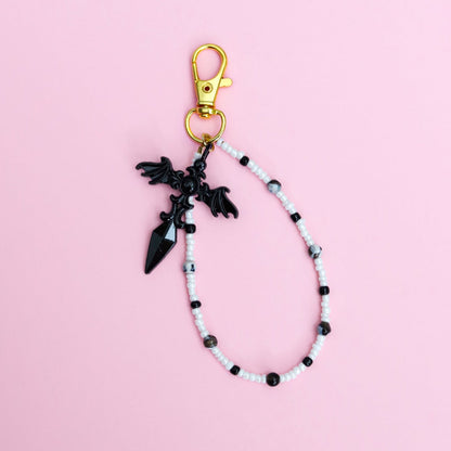 Keychain with black and white beads and black gothic cross pendant on a pink background