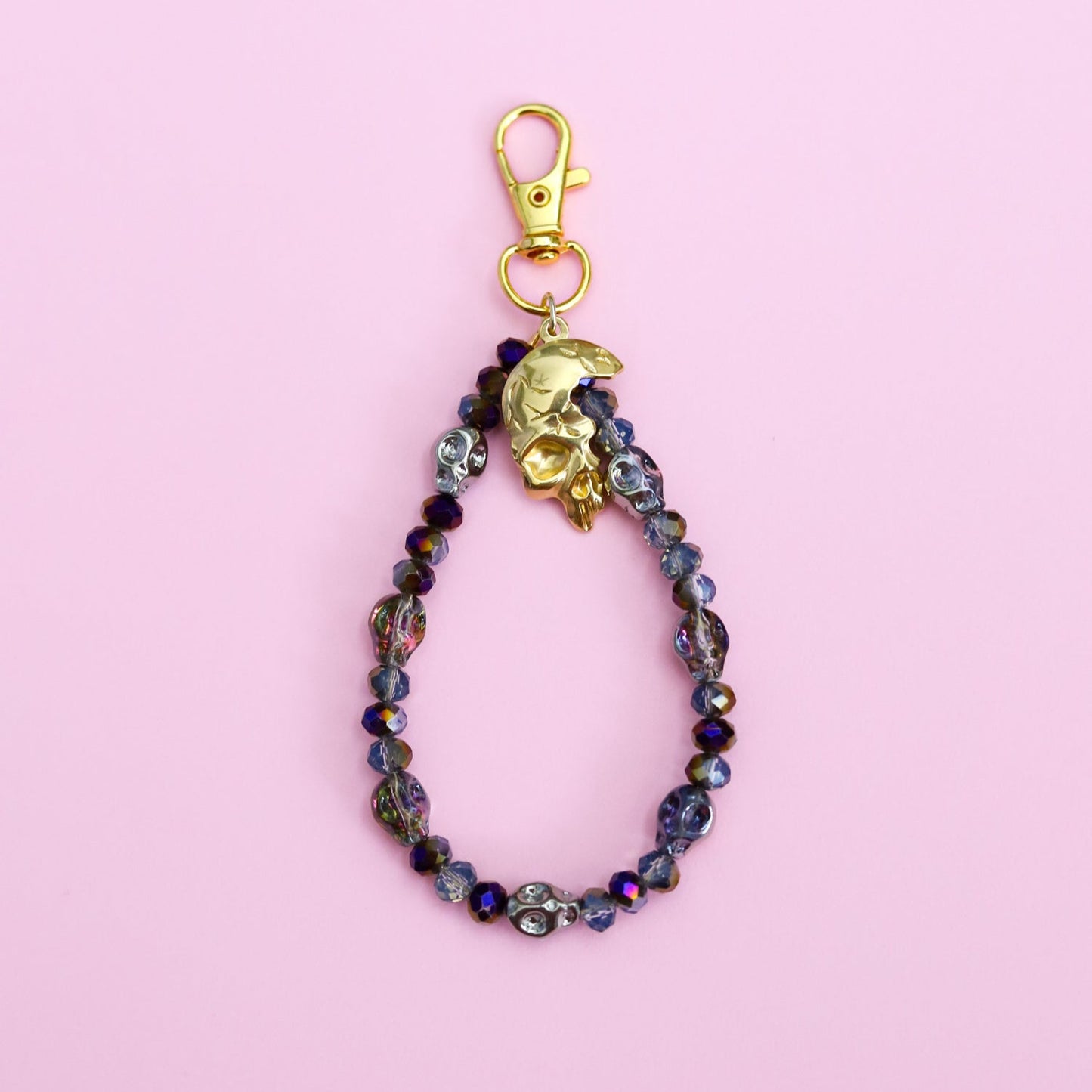 Beaded keychain with gold clasp on a pink background with skull beads and a skull pendant