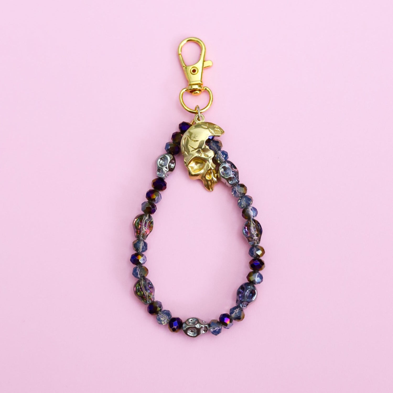 Beaded keychain with gold clasp on a pink background with skull beads and a skull pendant