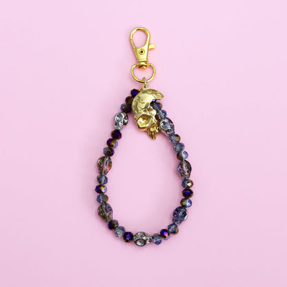 Beaded keychain with gold clasp on a pink background with skull beads and a skull pendant