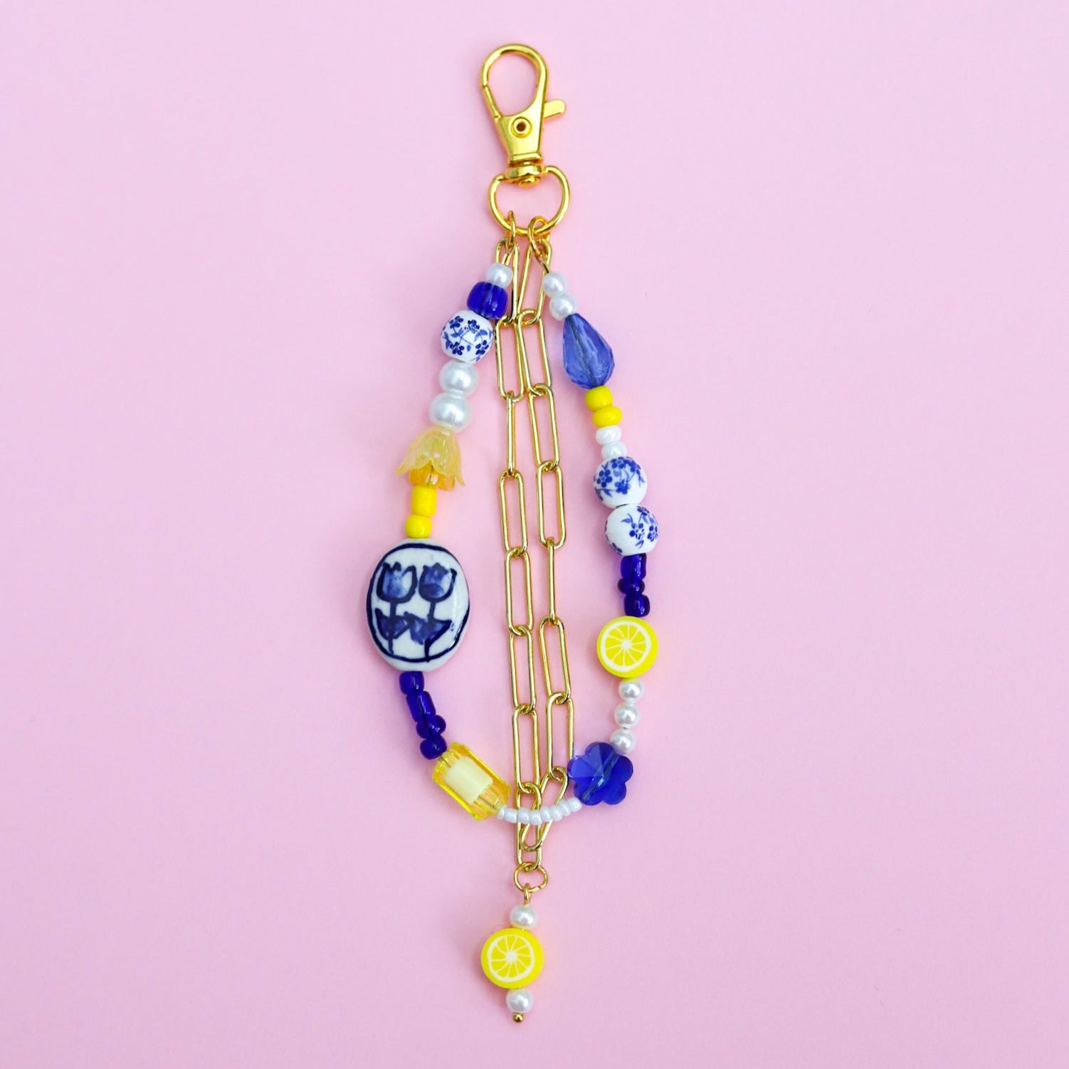 Blue, white, and yellow beaded keychain with gold chain on a pink background