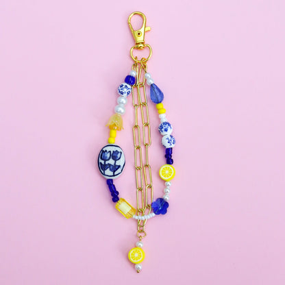 Blue, white, and yellow beaded keychain with gold chain on a pink background