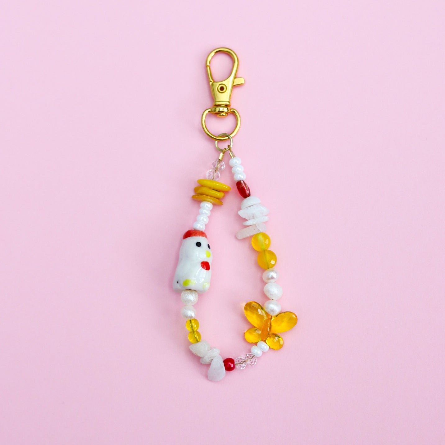 Keychain with assorted white, yellow, and red beads with a porcelain chicken bead on a pink background