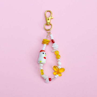 Keychain with assorted white, yellow, and red beads with a porcelain chicken bead on a pink background