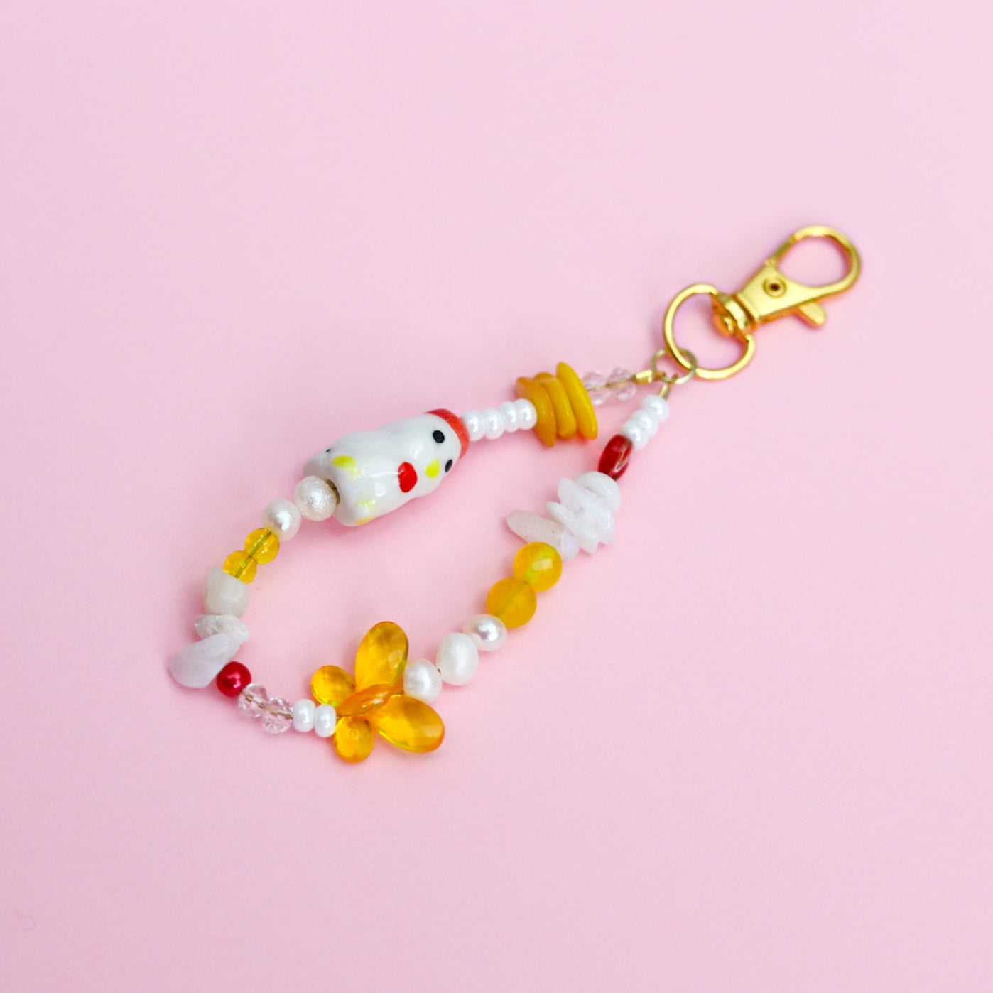 Keychain with assorted white, yellow, and red beads with a porcelain chicken bead on a pink background