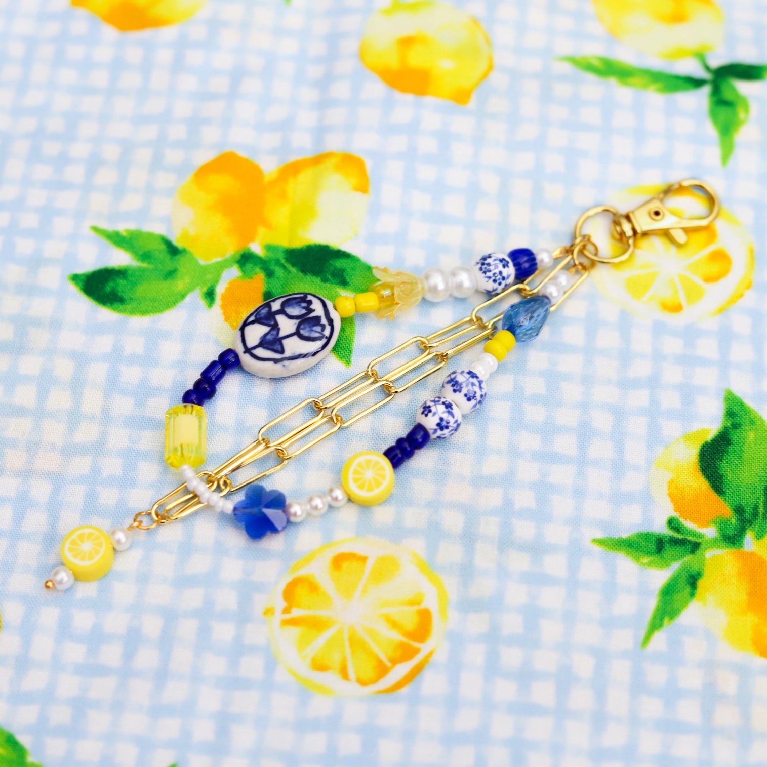 Blue, white, and yellow beaded keychain with gold chain on a fabric background with lemon designs