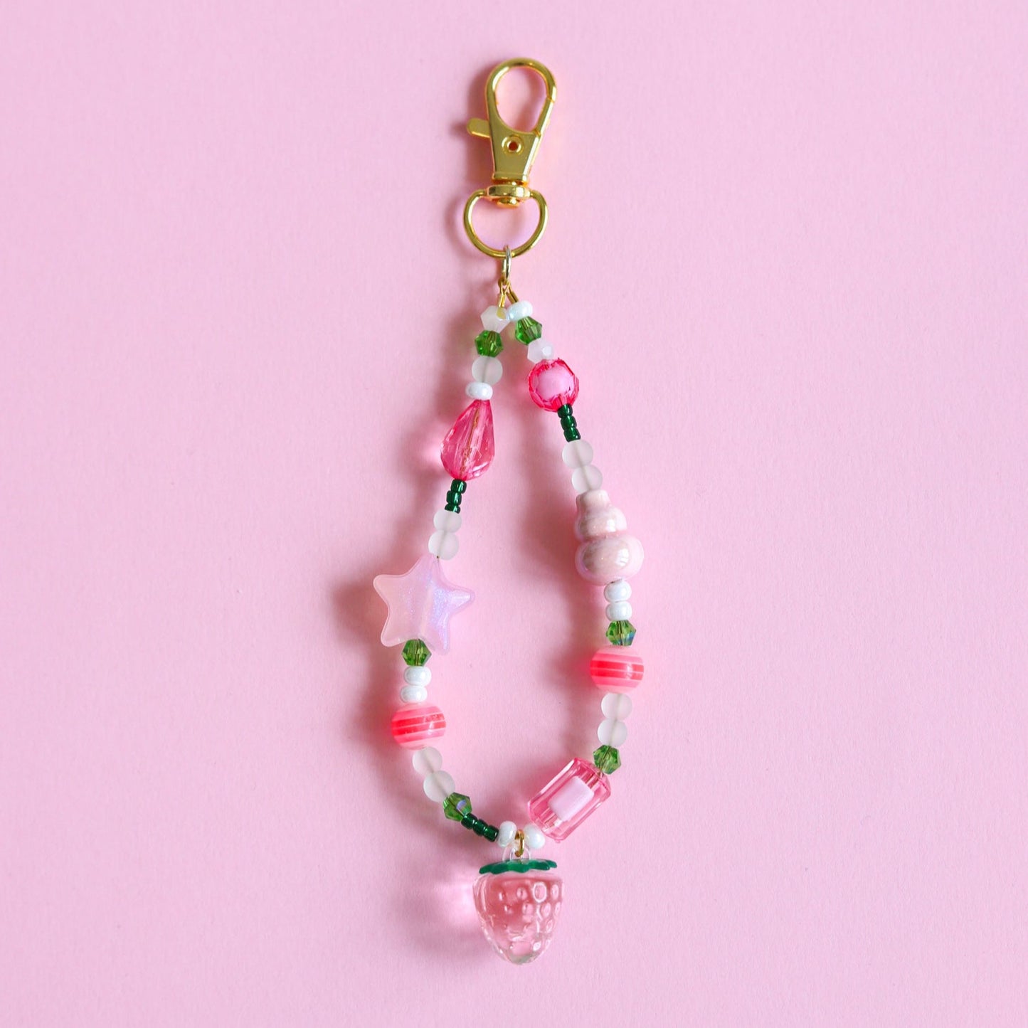 Beaded keychain with pink and green assorted beads and a light pink strawberry pendant hooked on a brown leather purse