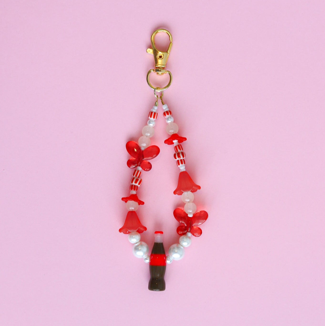 Keychain with assorted red and white beads, including red butterflies and a cola bottle, against a pink background