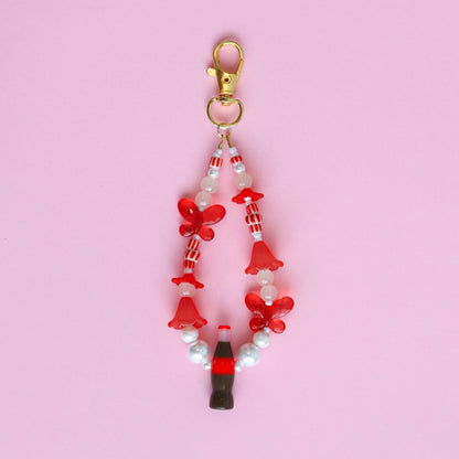 Keychain with assorted red and white beads, including red butterflies and a cola bottle, against a pink background
