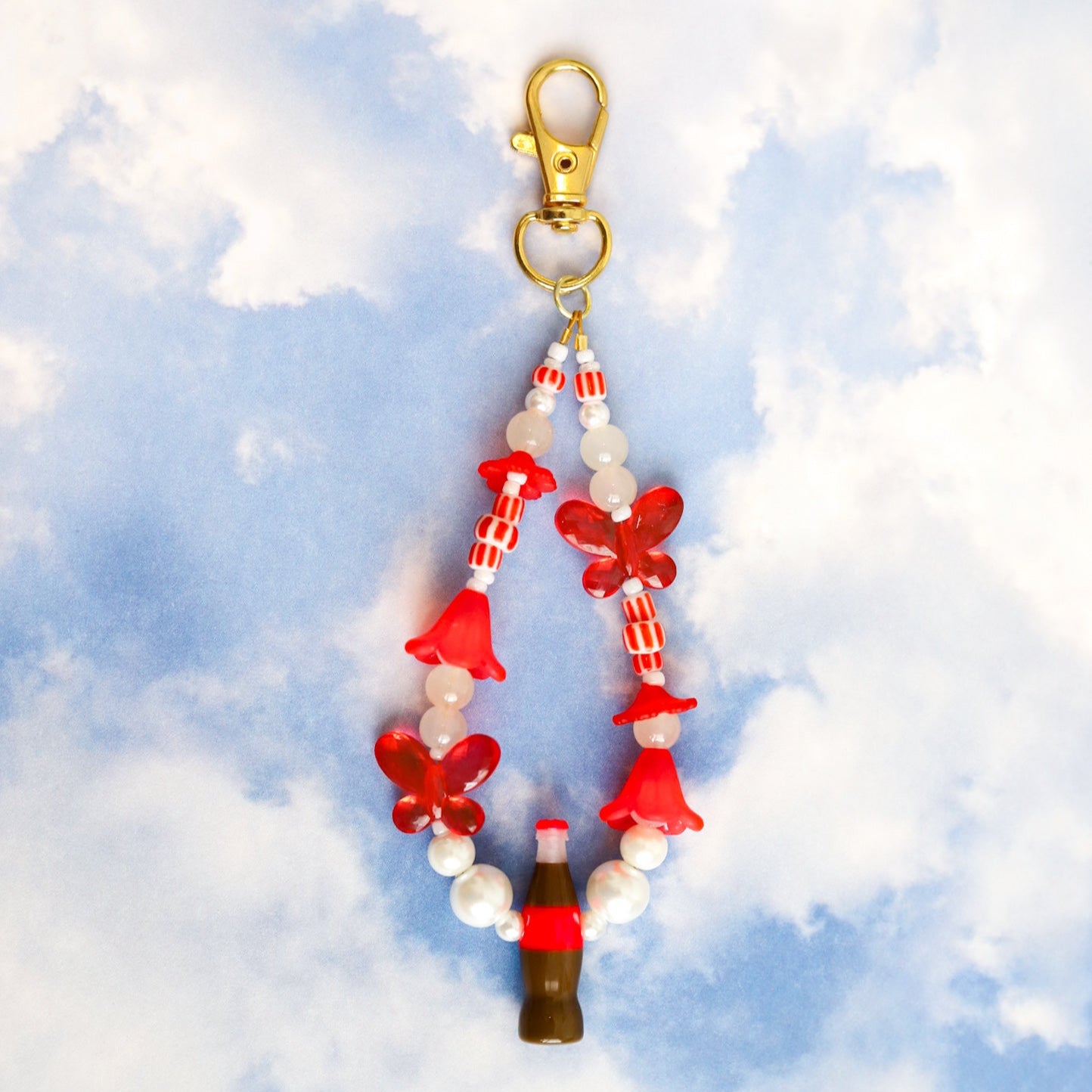 Keychain with assorted red and white beads, including red butterflies and a cola bottle, against a cloudy sky background