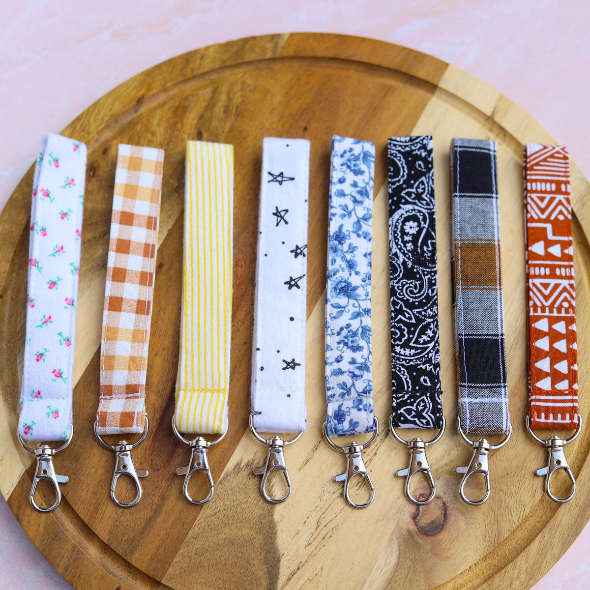 Set of patterned keychains on a wooden plate with a pink background