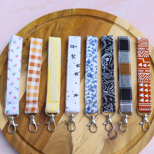 Set of patterned keychains on a wooden plate with a pink background